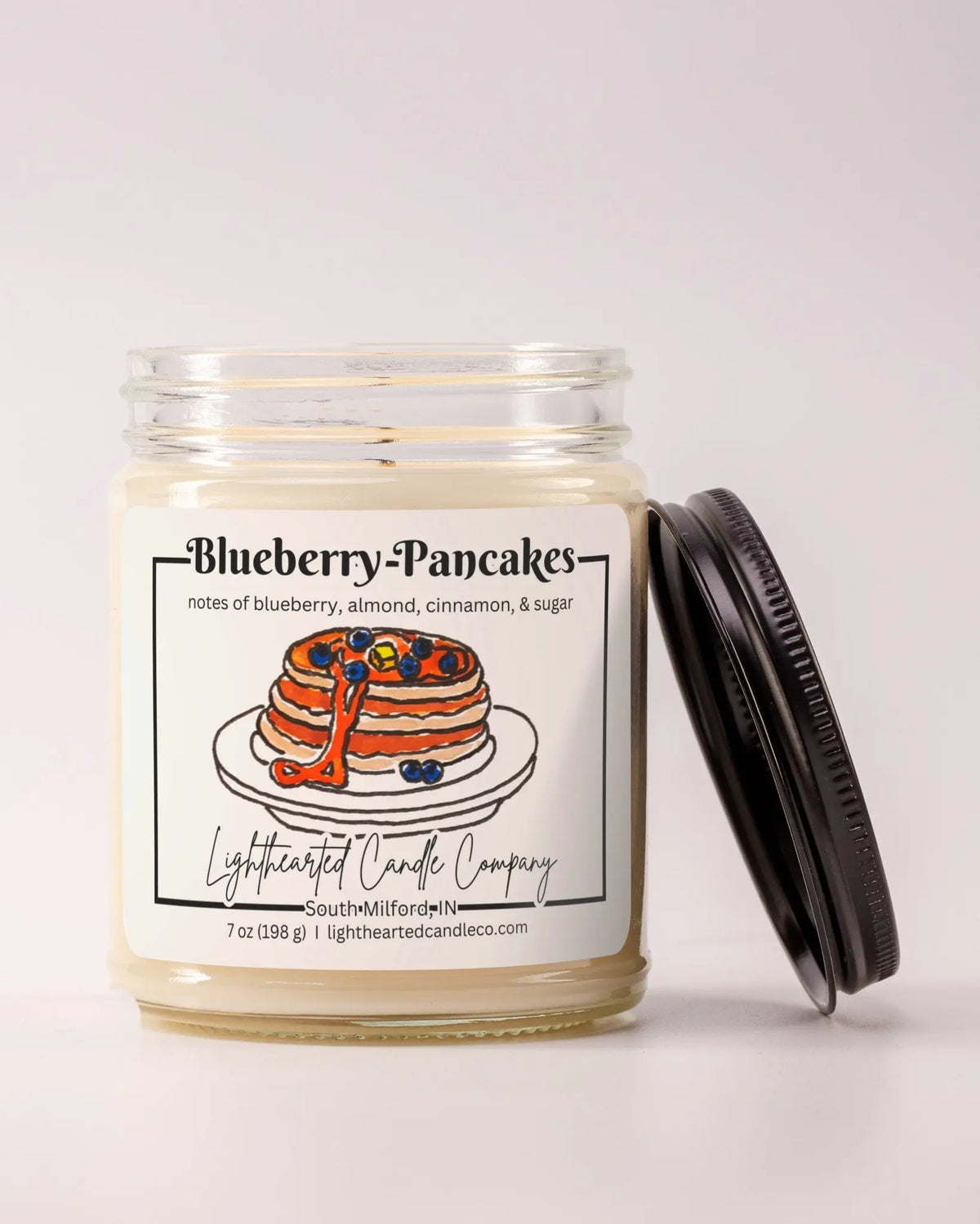 Unlit Blueberry Pancakes Candle in a clear glass jar with its black lid beside it