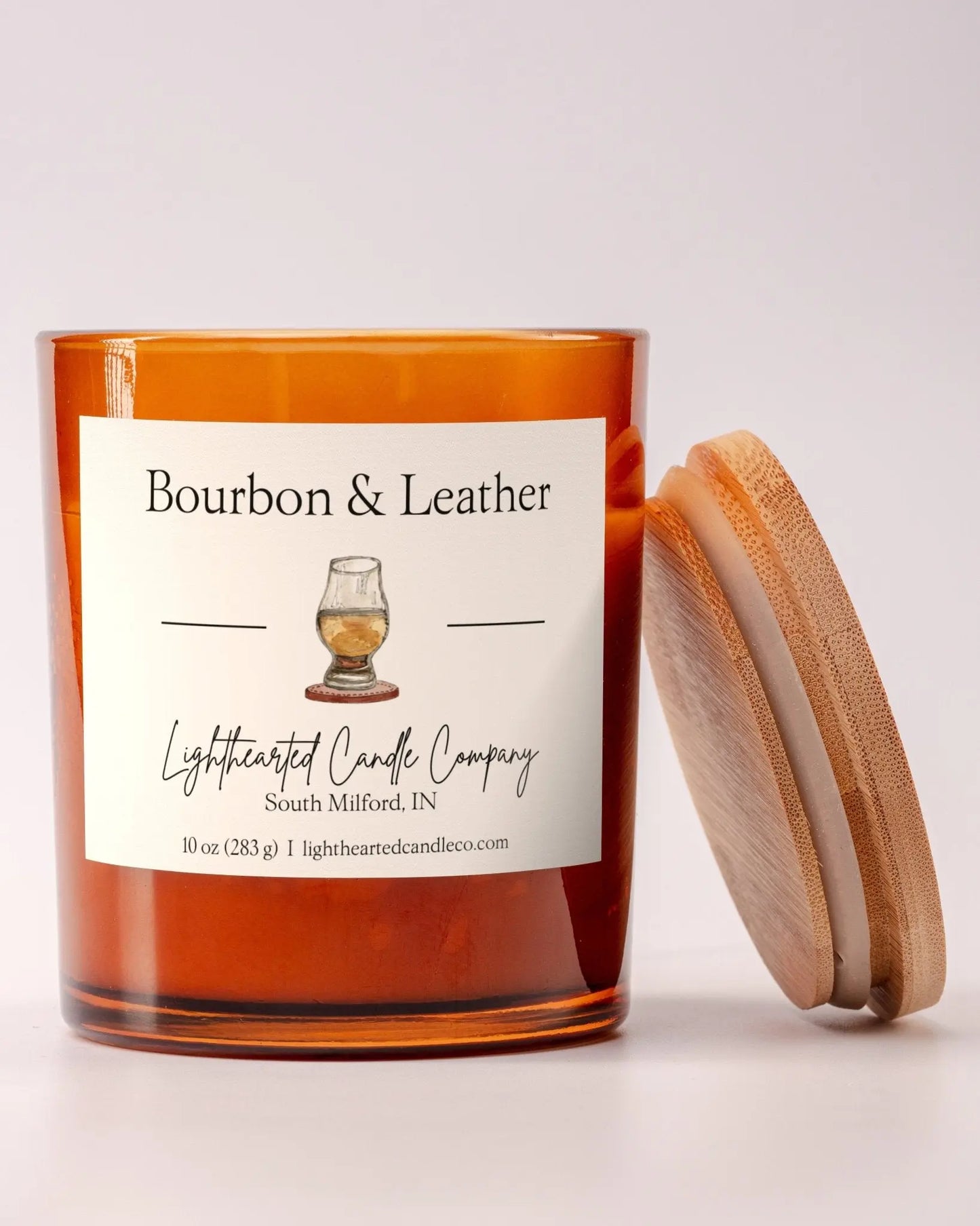 Unlit Bourbon & Leather Candle in an amber glass jar with its wooden lid beside it