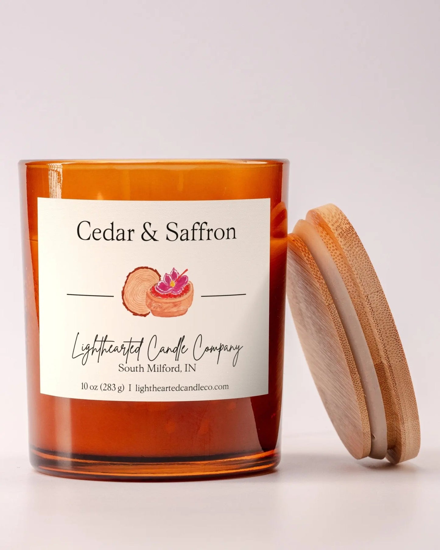 Lit Cedar & Saffron Candle in an amber glass jar with its wooden lid leaning beside it