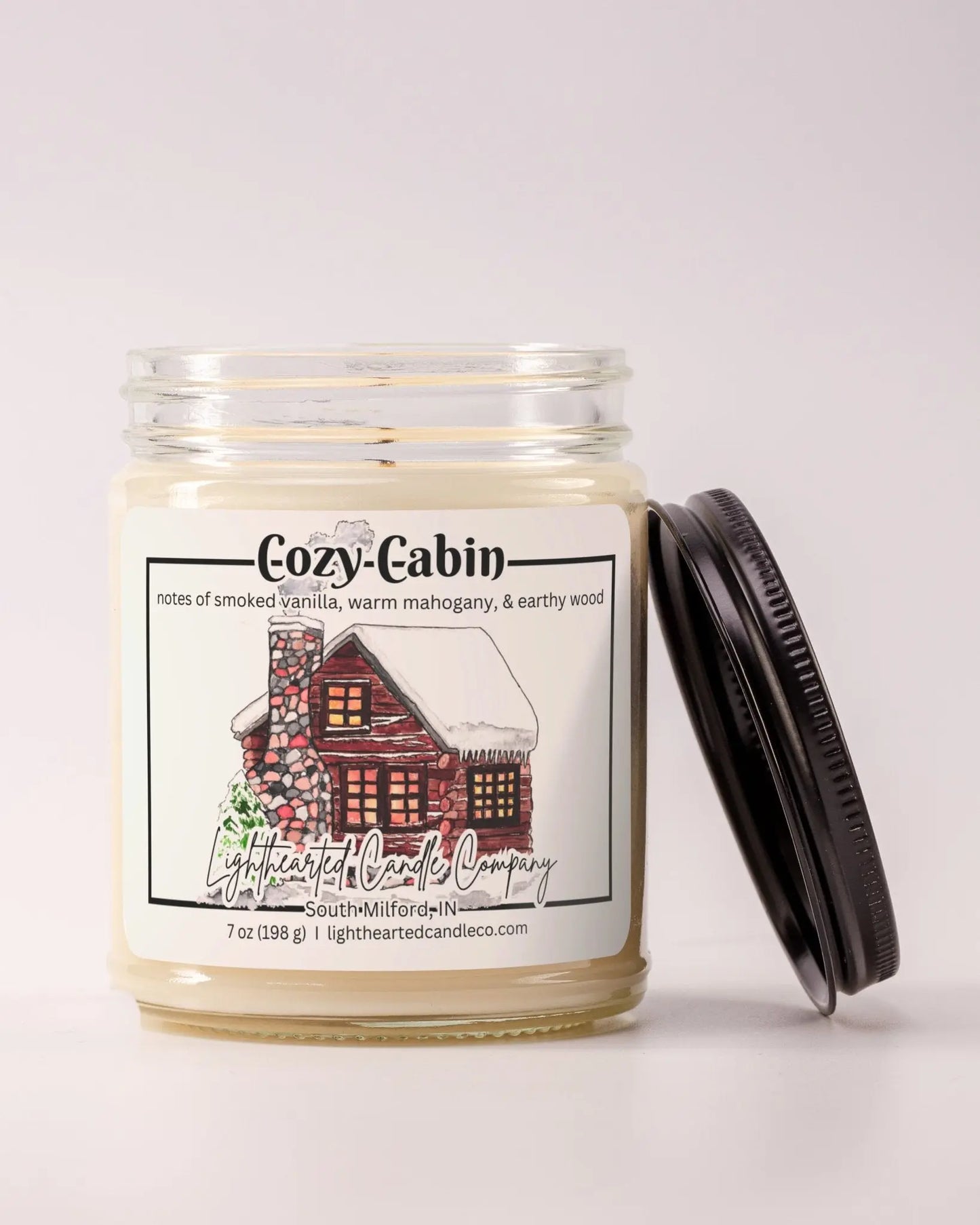 Unlit Cozy Cabin Candle in a clear glass jar with its black lid beside it