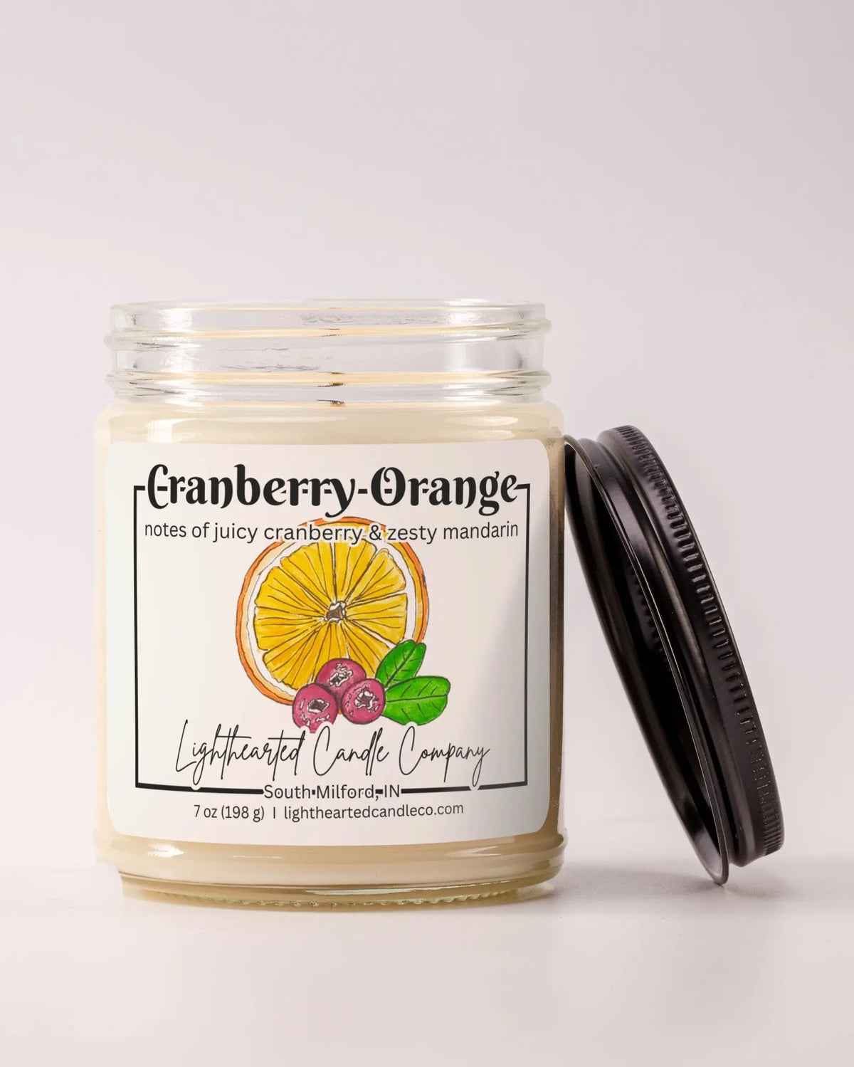 Unlit Cranberry Orange Candle in a clear glass jar with its black lid beside it