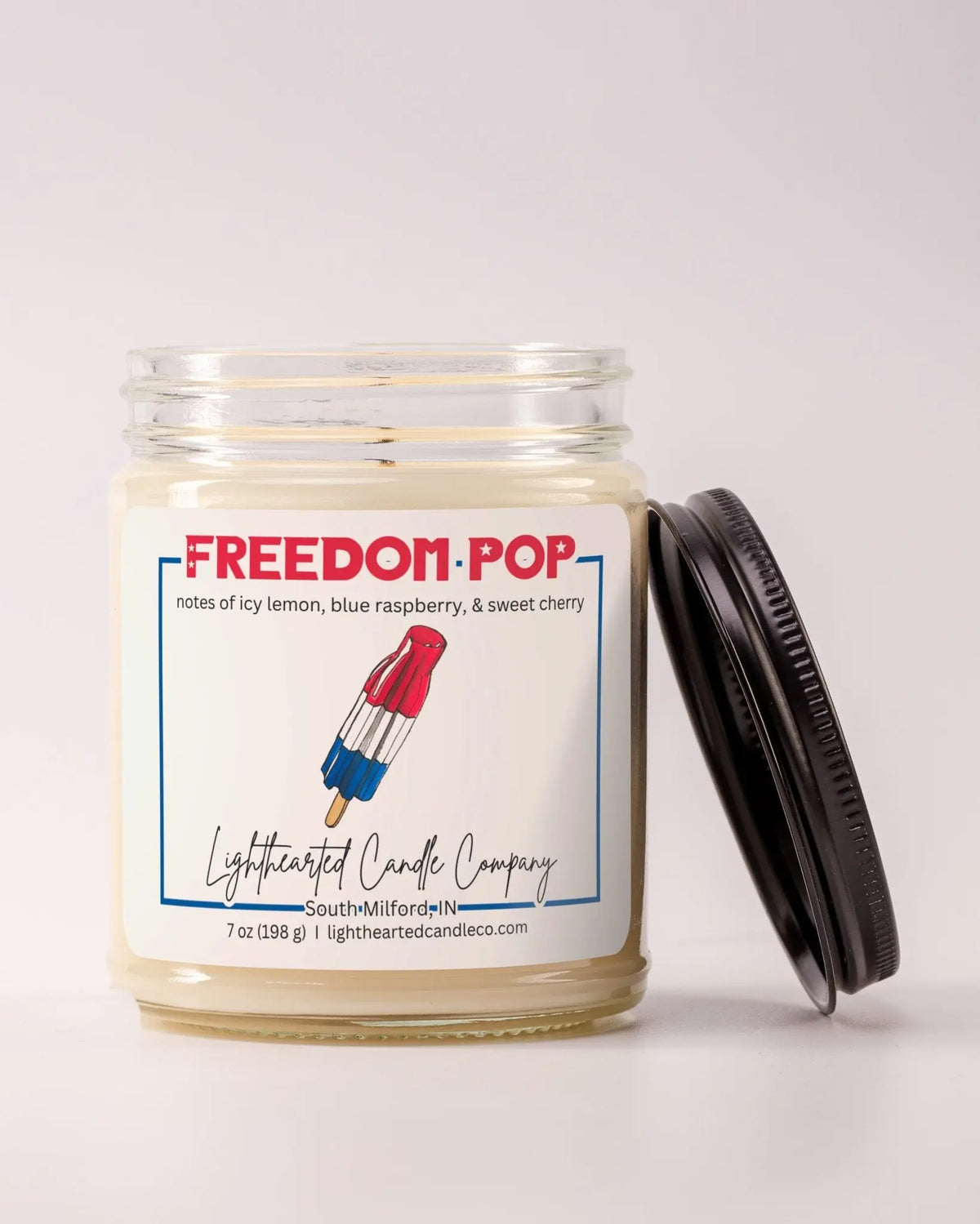 Unlit Freedom Pop Candle in a clear glass jar with its black lid beside it