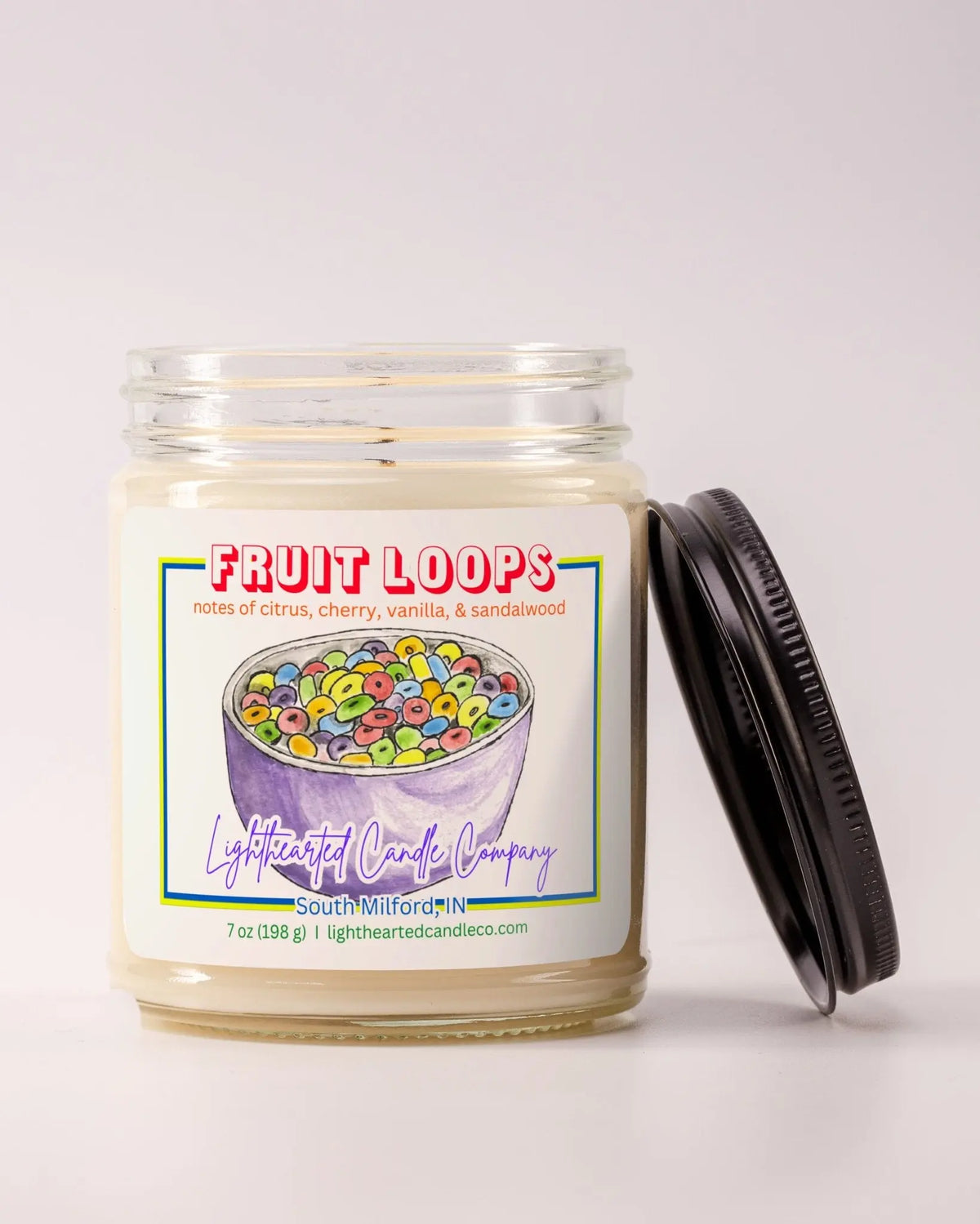 Unlit Fruit Loops Candle in a clear glass jar with its black lid beside it