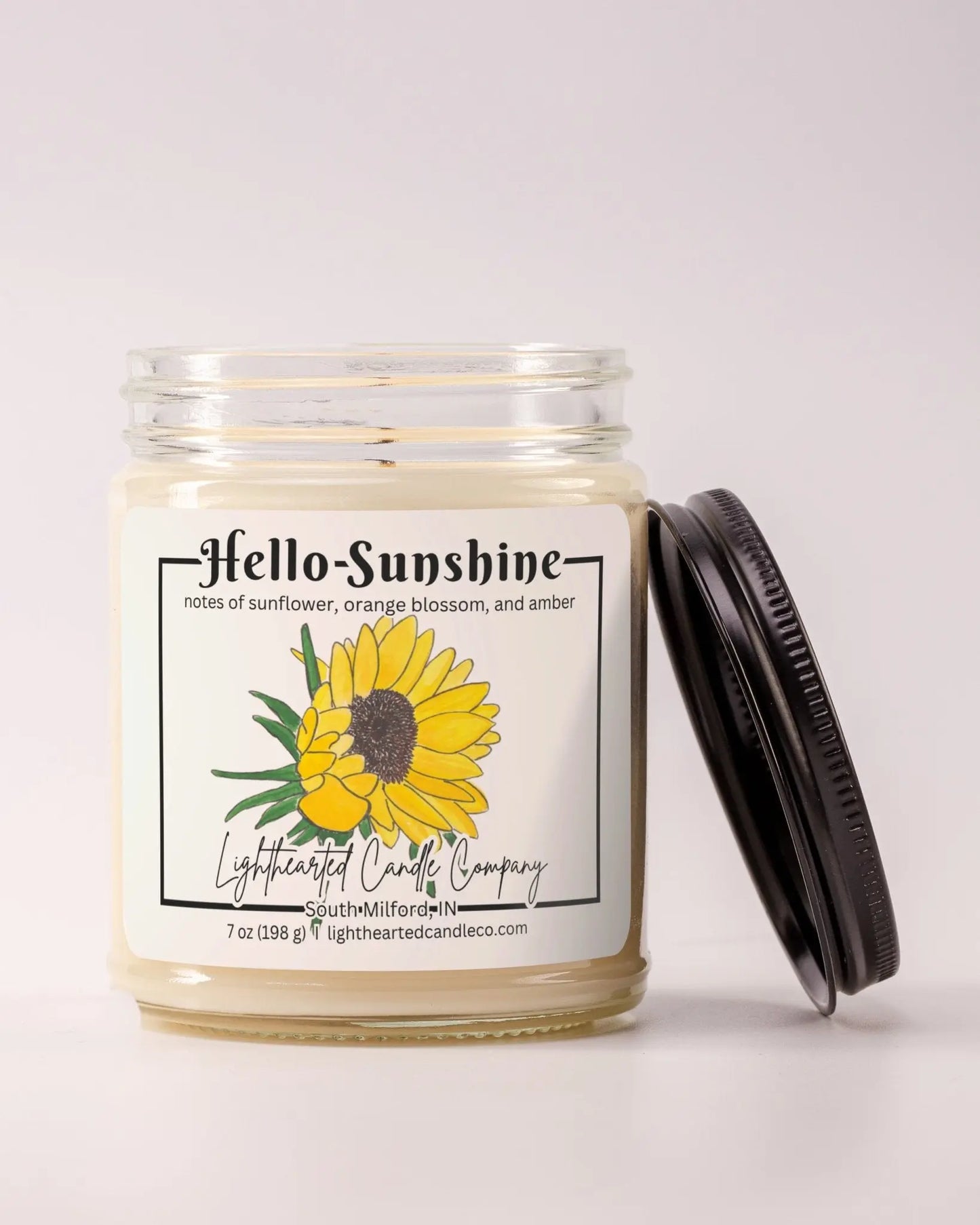 Unlit Hello Sunshine Candle in a clear glass jar with its black lid beside it