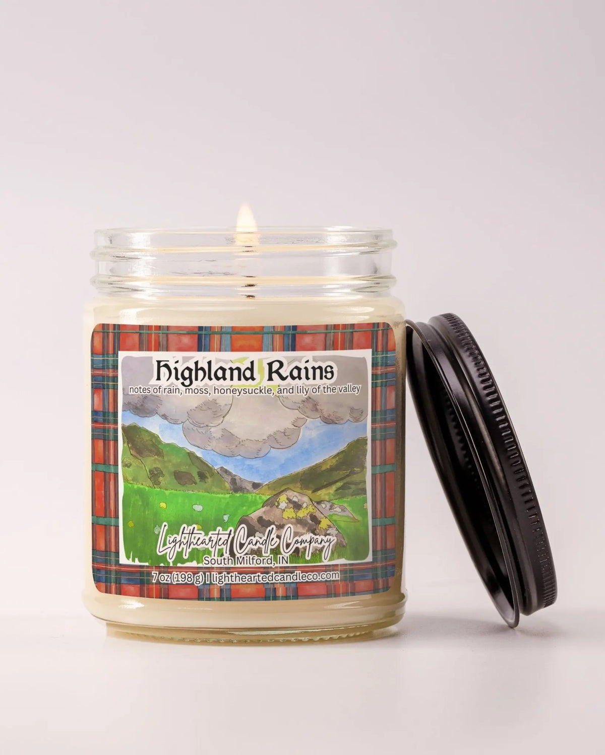 Lit Highland Rains Candle in a clear glass jar with its black lid beside it