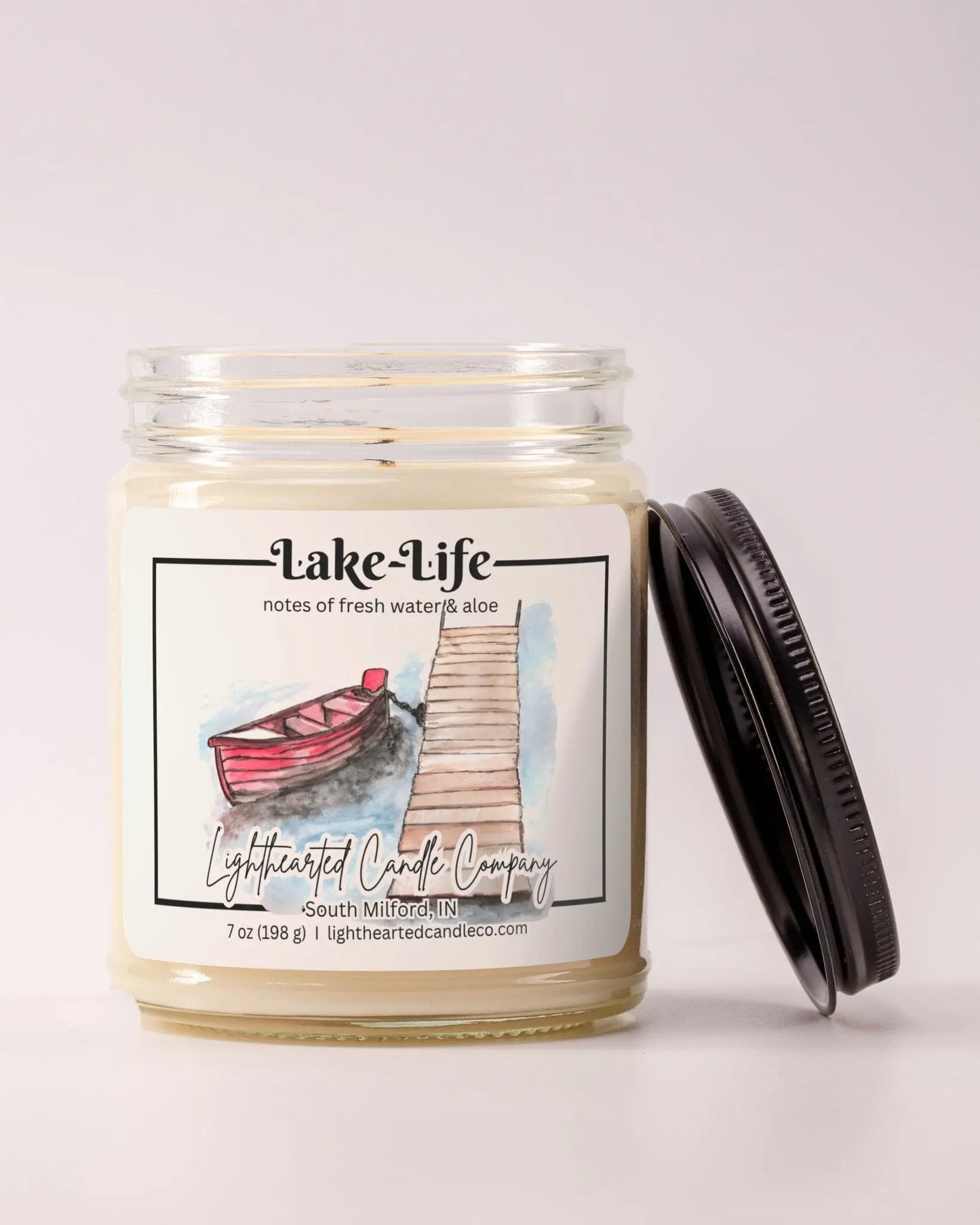 Unlit Lake Life Candle in a clear glass jar with its black lid beside it