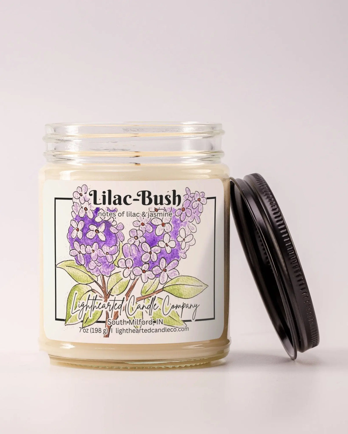 Unlit Lilac Bush Candle in a clear glass jar with its black lid beside it