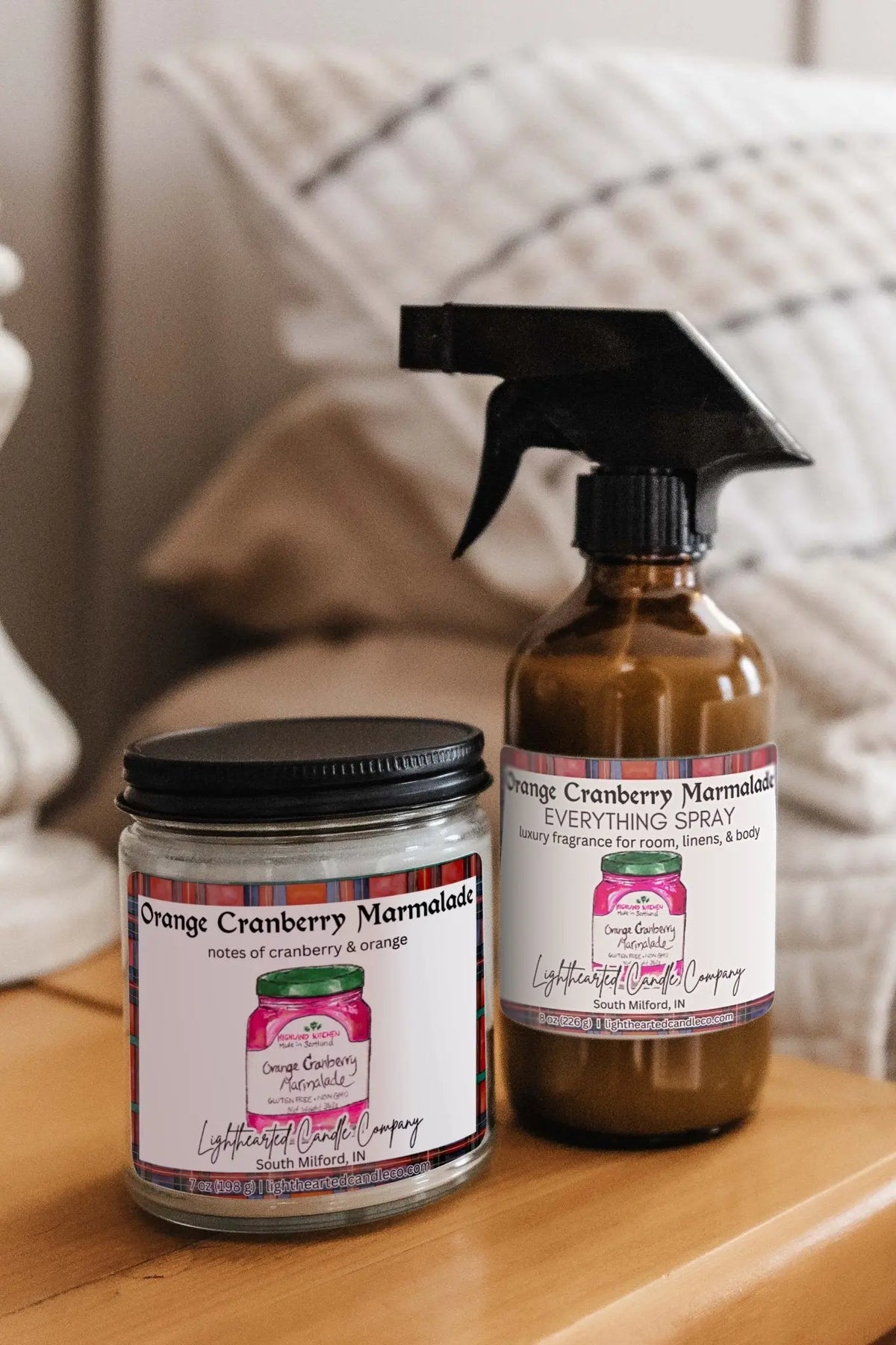 Matching candle and Orange Cranberry Marmalade Everything Spray styled on a bedside table
