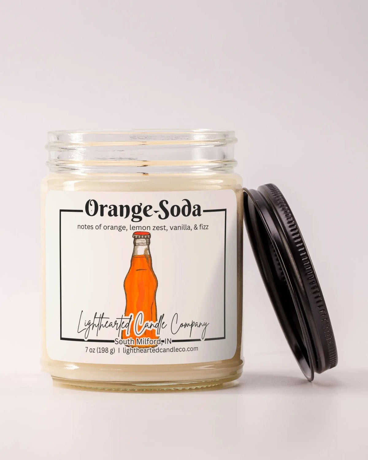 Unlit Orange Soda Candle in a clear glass jar with its black lid beside it
