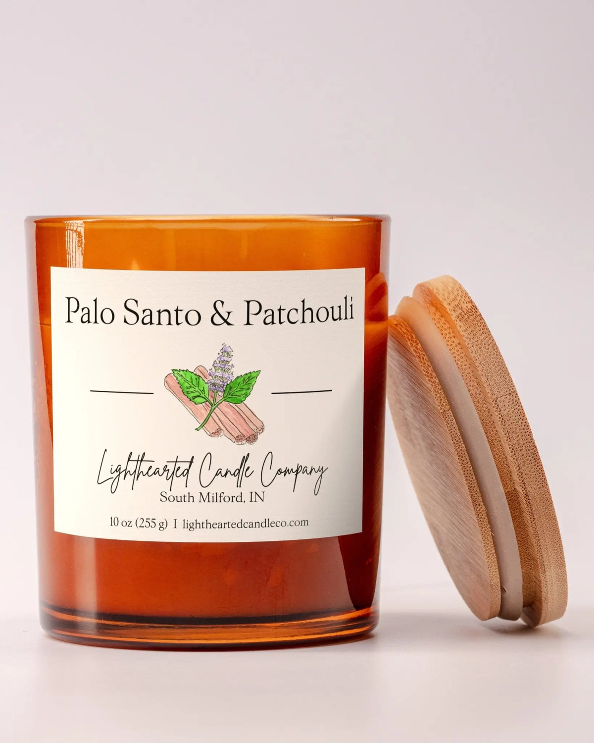 Lit Palo Santo & Patchouli Candle in an amber glass jar with its wooden lid leaning beside it