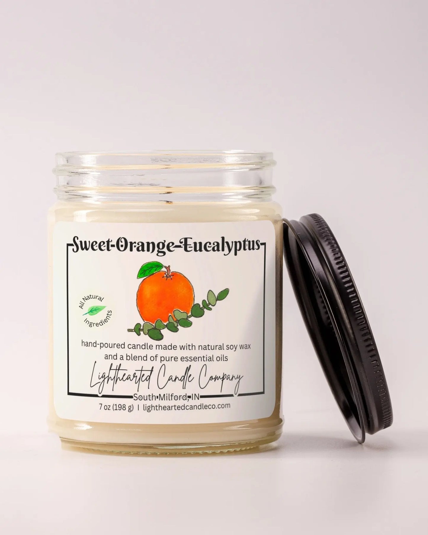 Unlit Sweet Orange Eucalyptus Essential Oil Candle in a clear glass jar with its black lid beside it