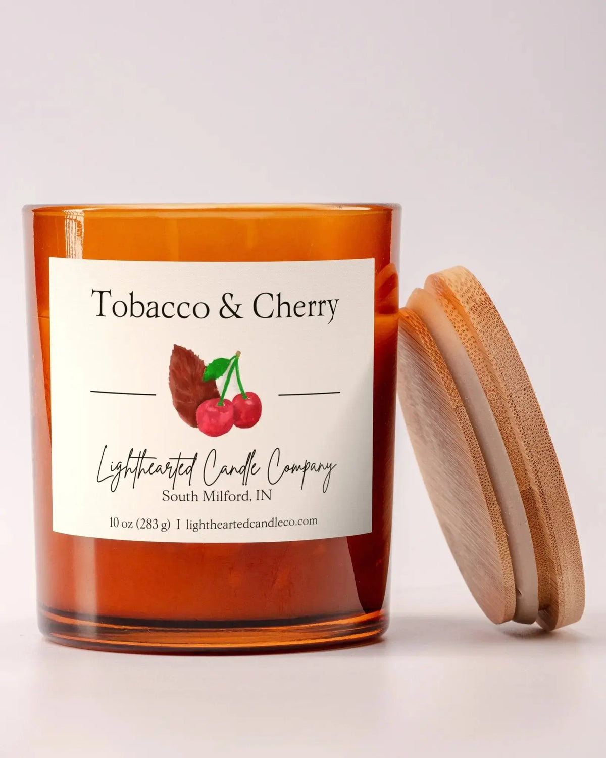 Unlit Tobacco & Cherry Candle in an amber glass jar with its wooden lid beside it