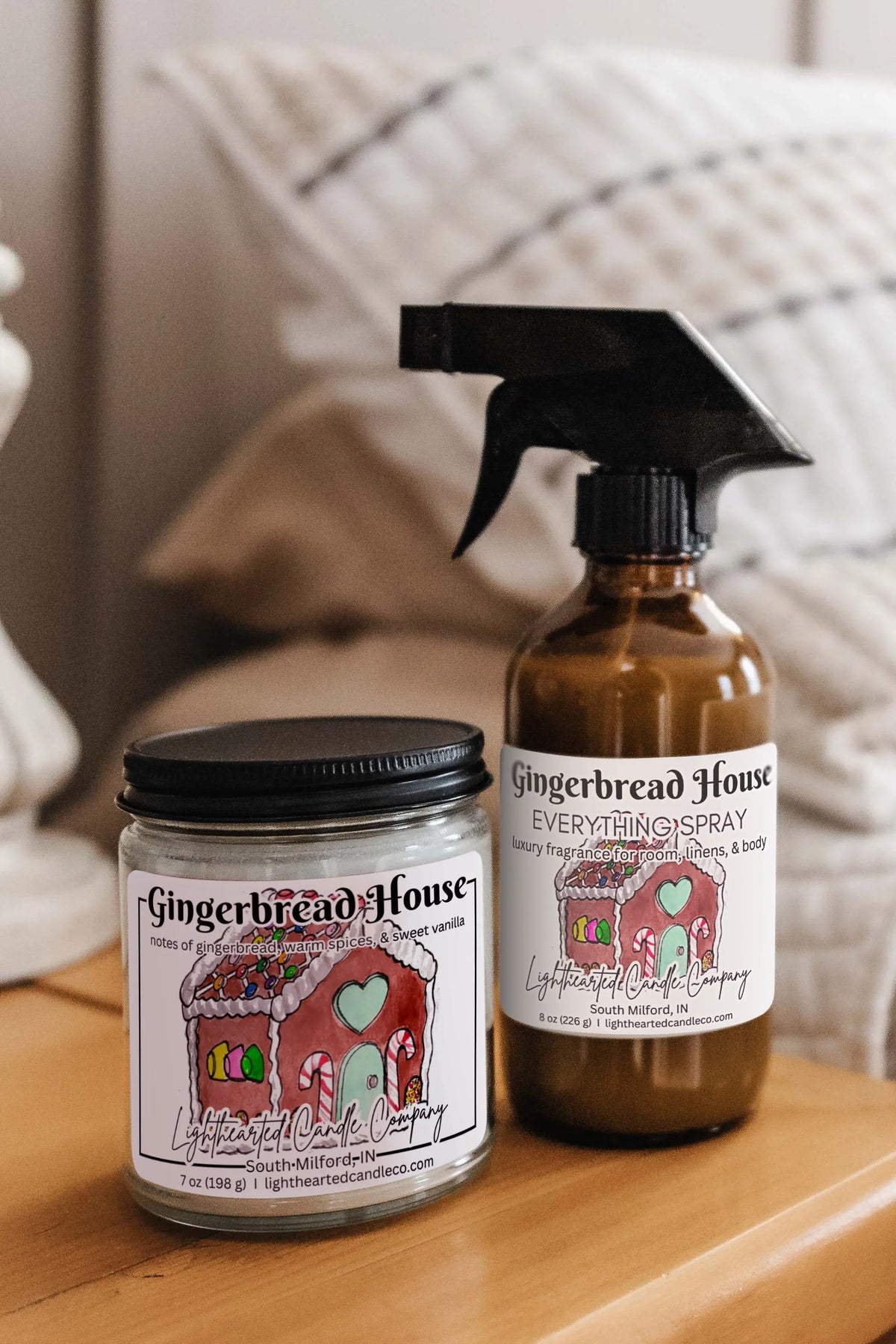 Matching candle and Gingerbread House Everything Spray styled on a bedside table