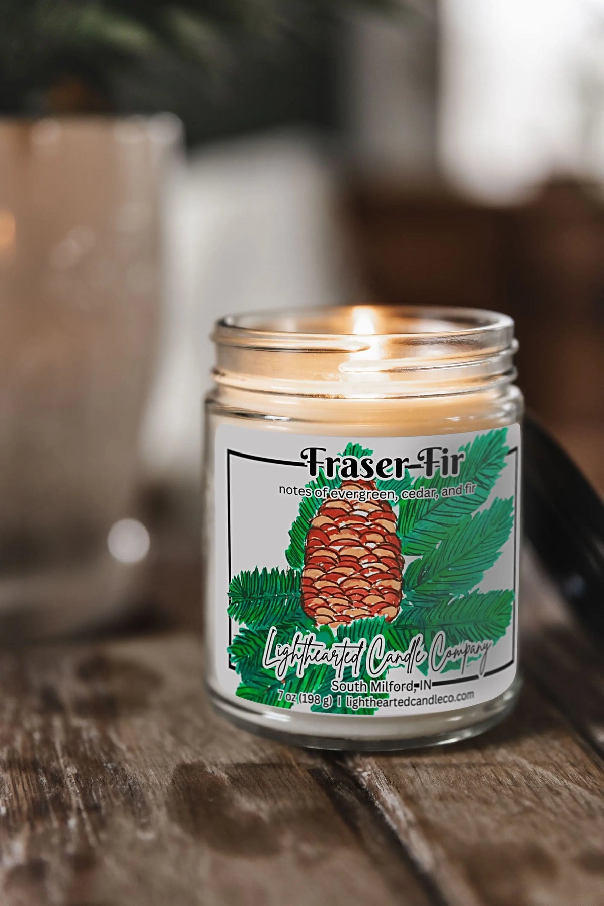 Lit Fraser Fir Candle in a clear glass jar on a rustic wooden table