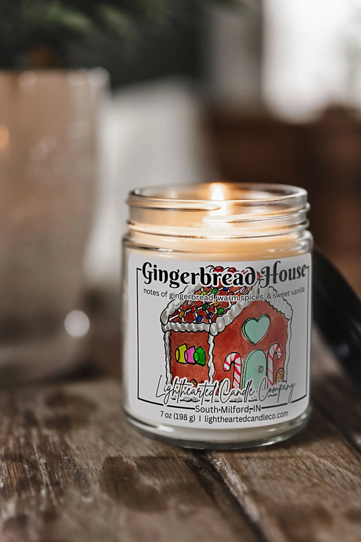 Lit Gingerbread House Candle in a clear glass jar with original watercolor artwork and a metal lid