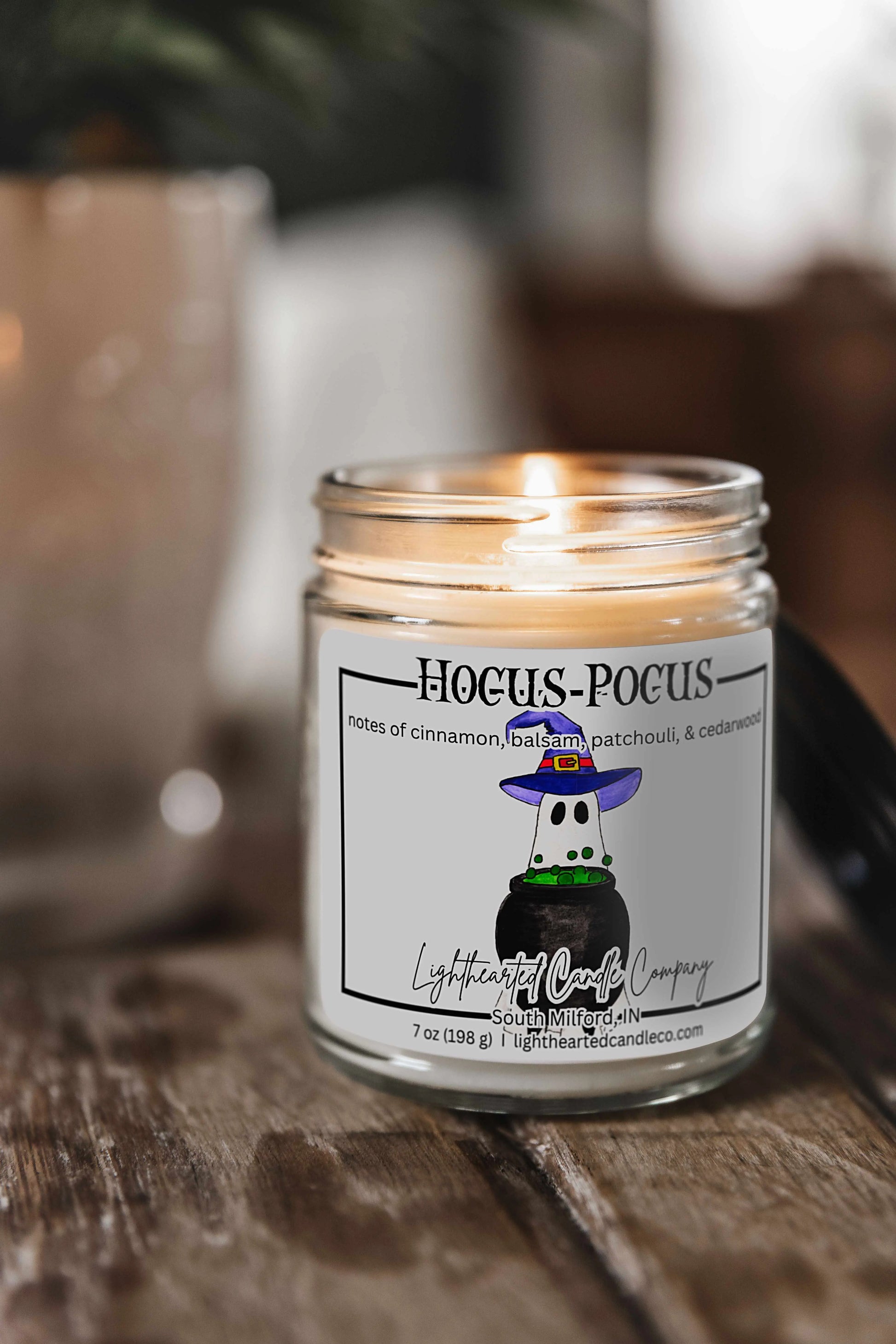 Lit Hocus Pocus Candle in a clear glass jar on a rustic wooden table