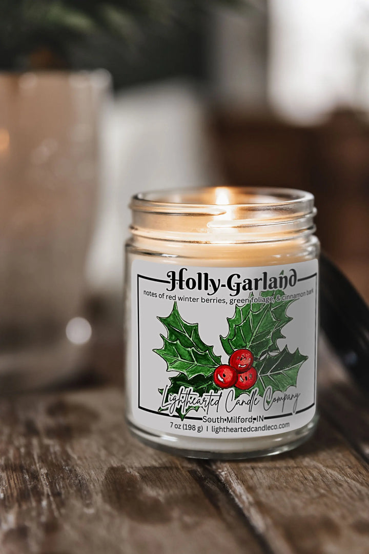 Lit Holly Garland Candle in a clear glass jar with original watercolor artwork and a metal lid