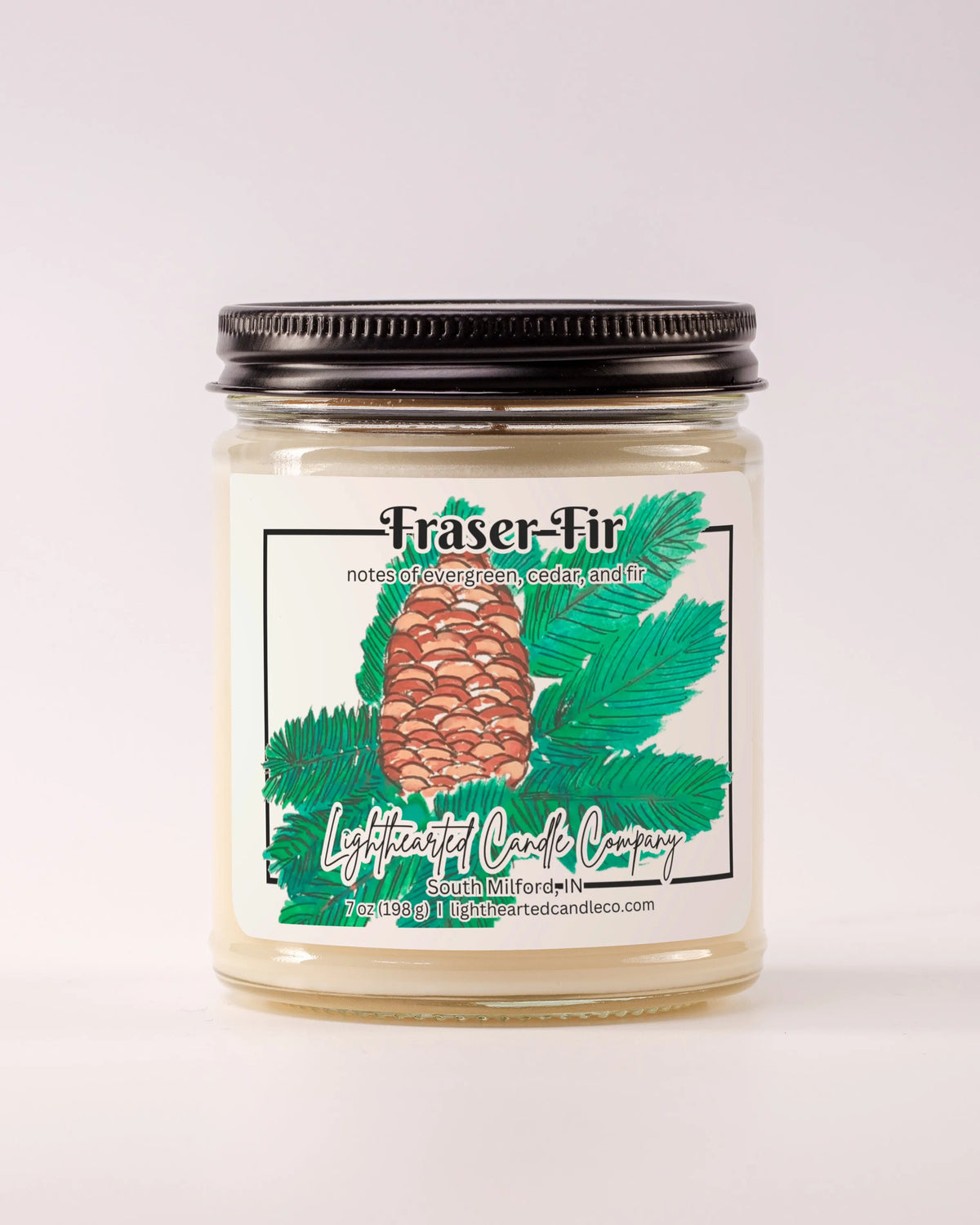 Lit Fraser Fir Candle in a clear glass jar with its black lid beside it