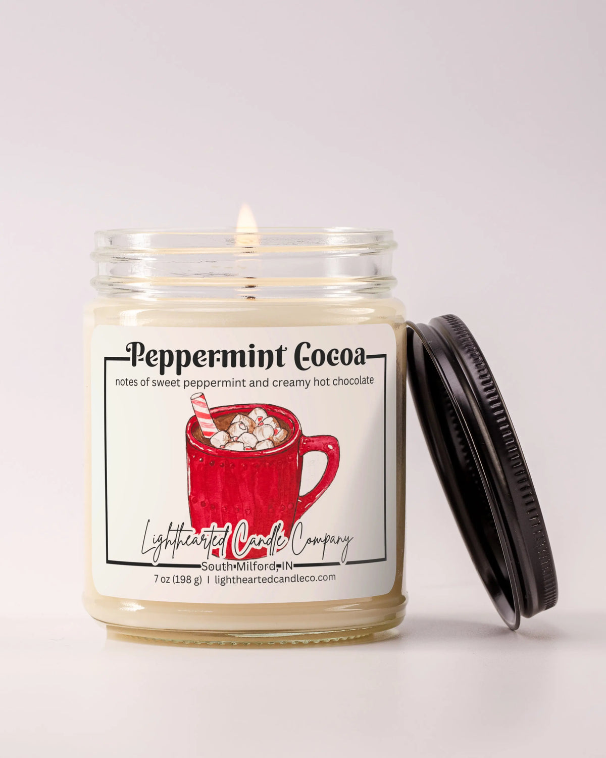 Lit Peppermint Cocoa Candle in a clear glass jar with its black lid beside it