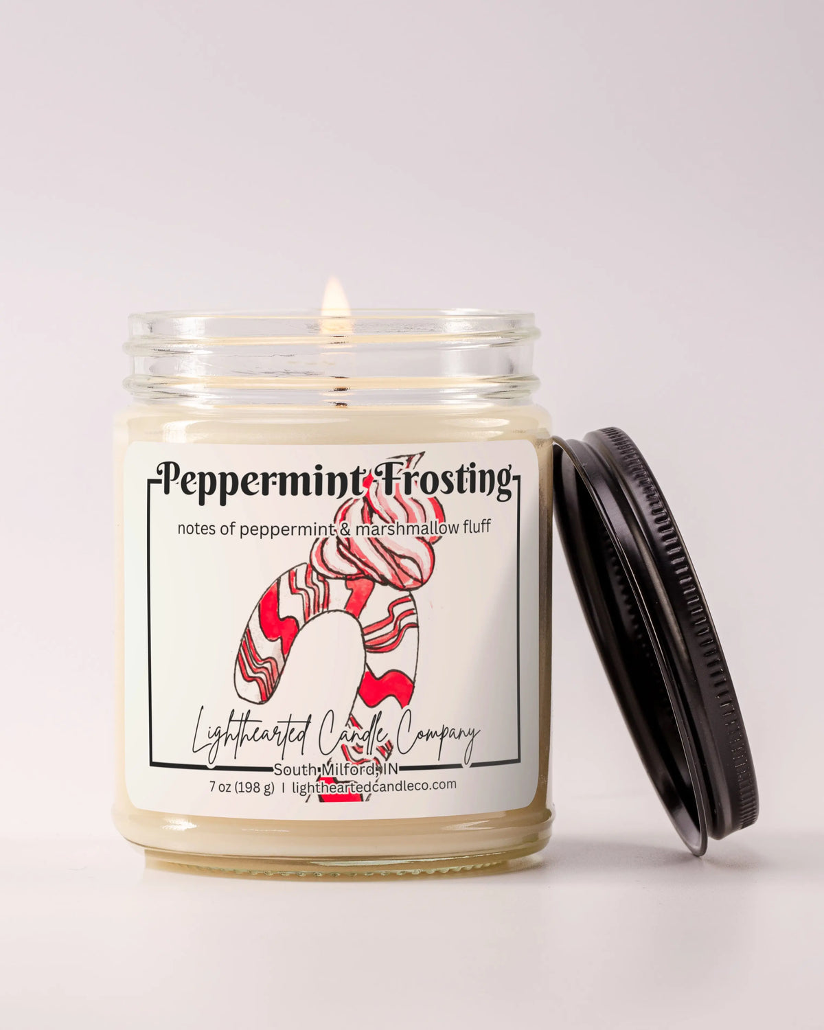 Lit Peppermint Frosting Candle in a clear glass jar with its black lid beside it