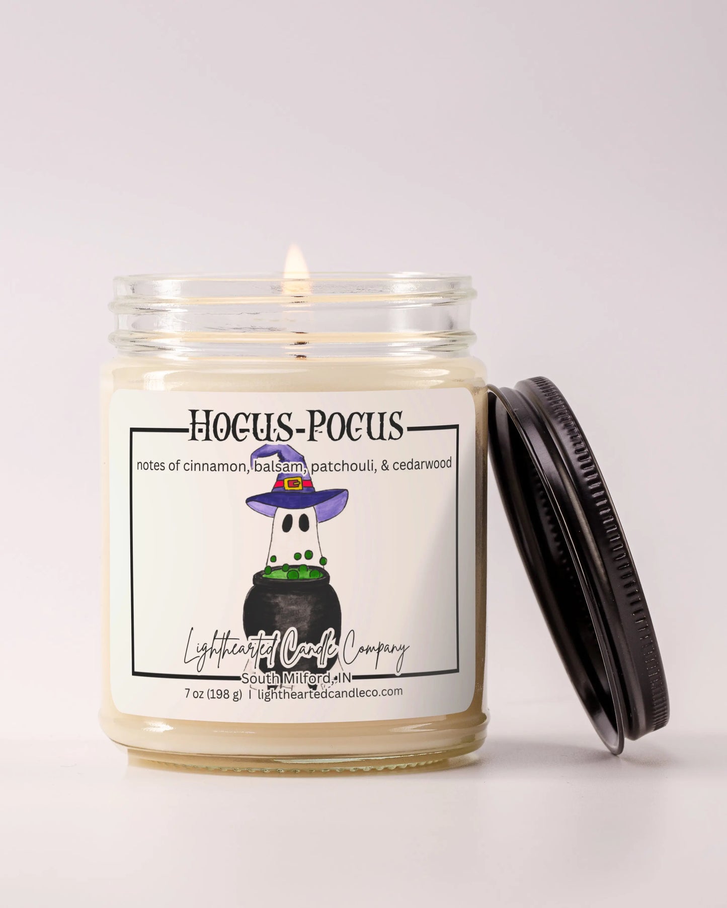 Lit Hocus Pocus Candle in a clear glass jar with its black lid beside it, alternate view 3