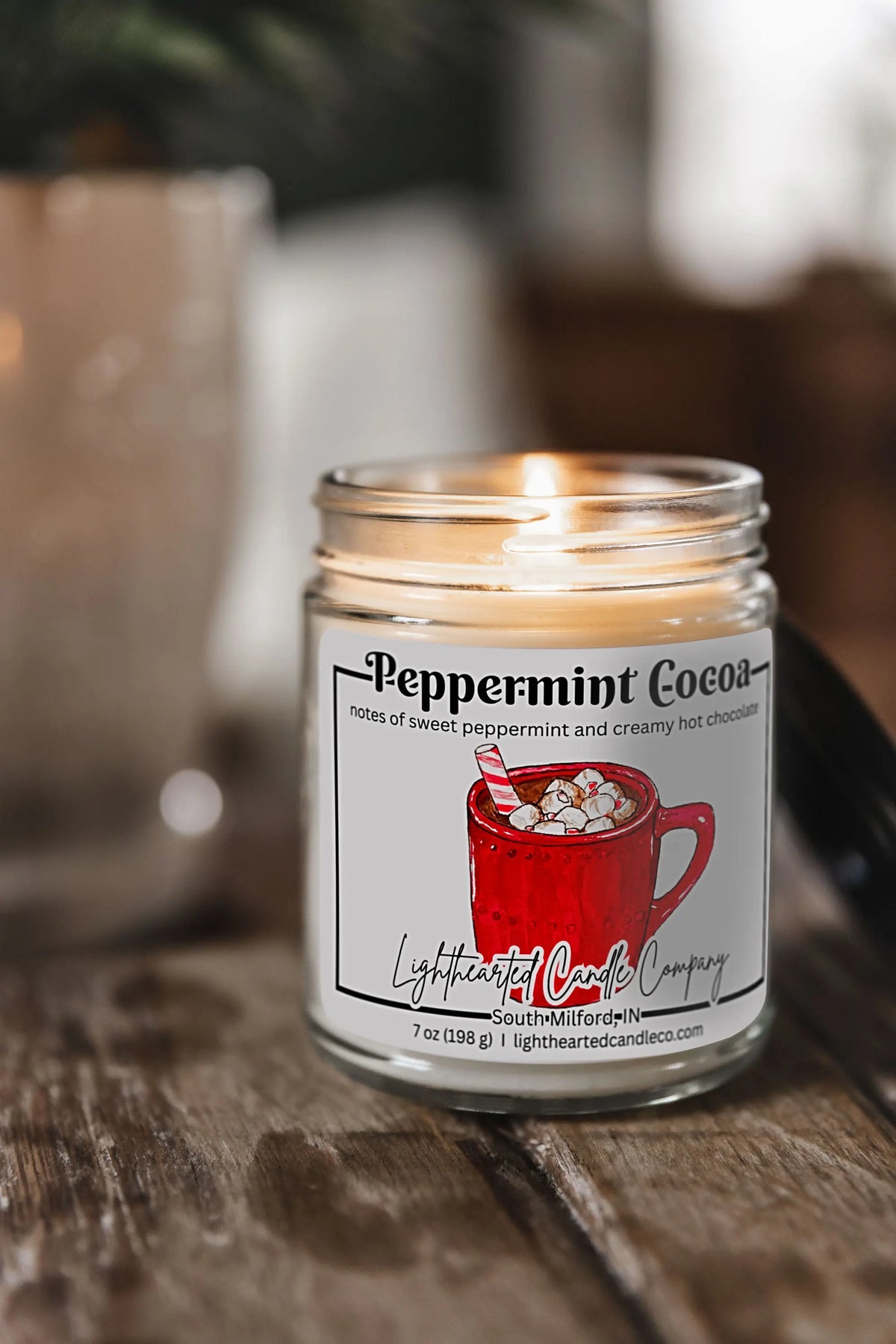 Lit Peppermint Cocoa Candle in a clear glass jar on a rustic wooden table