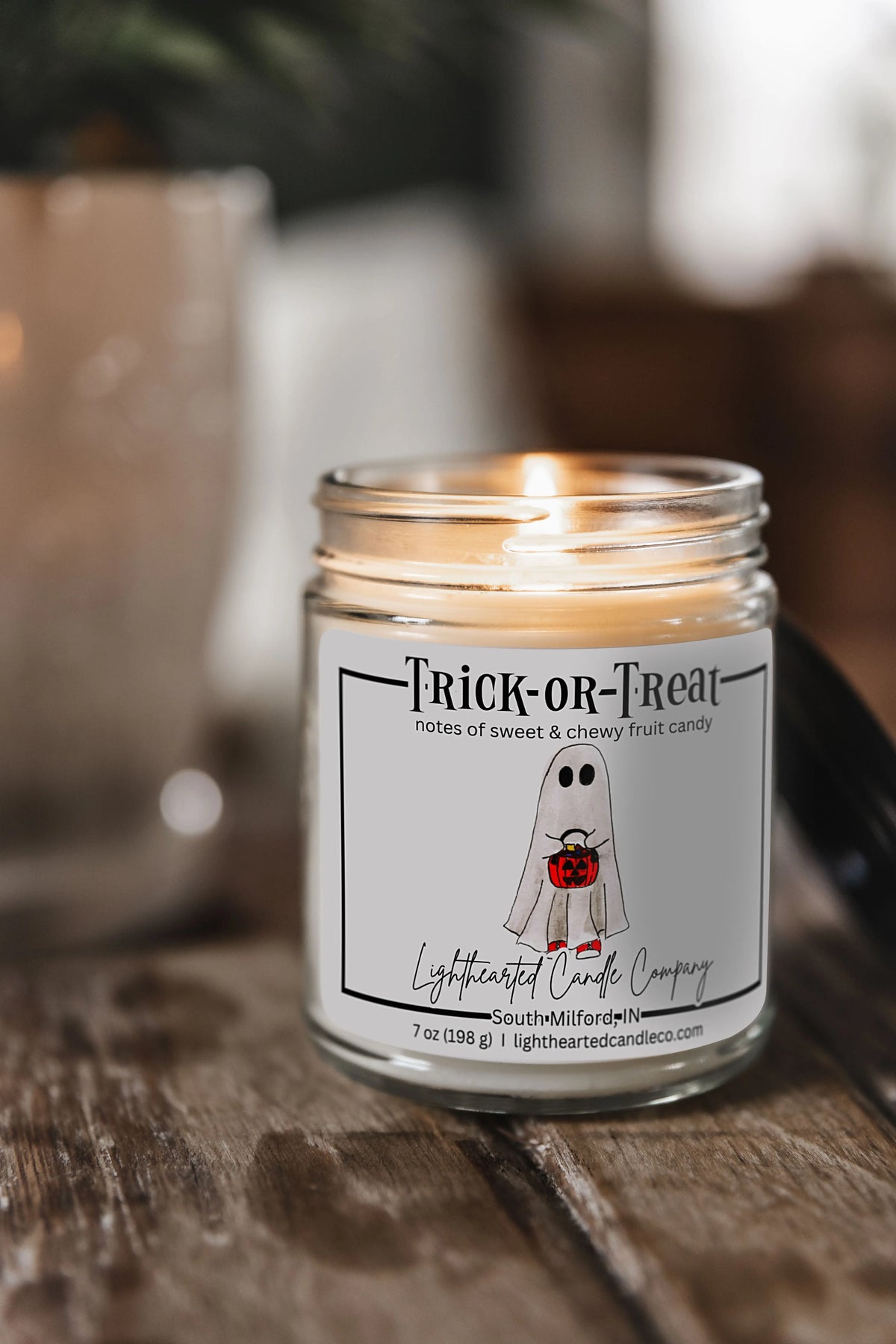 Lit Trick or Treat Candle in a clear glass jar on a rustic wooden table