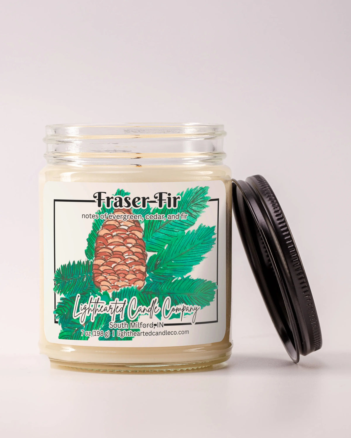 Unlit Fraser Fir Candle in a clear glass jar with its black lid beside it