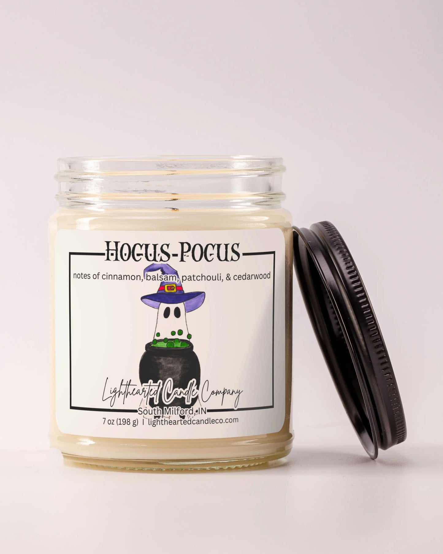 Unlit Hocus Pocus Candle in a clear glass jar with its black lid beside it