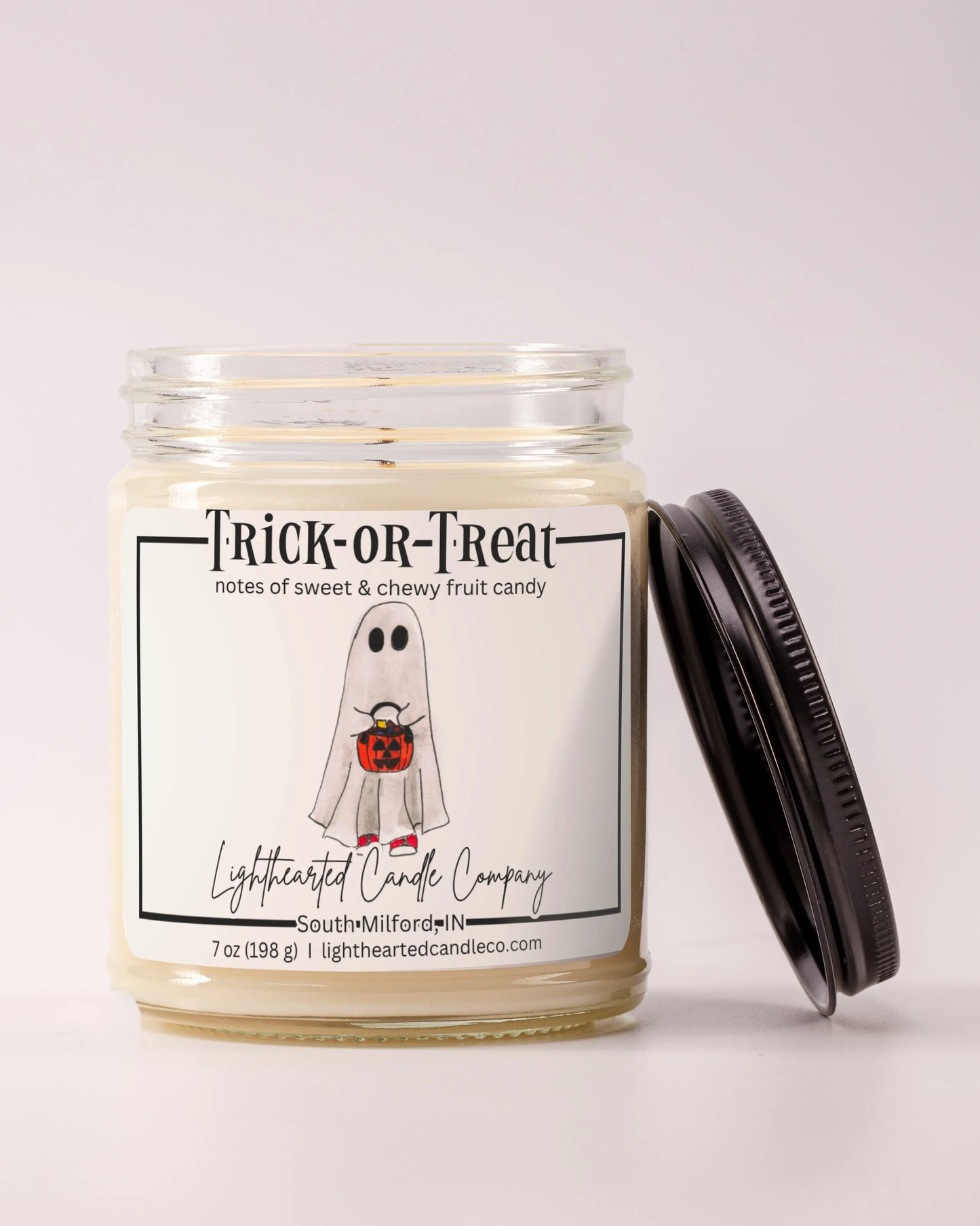 Unlit Trick or Treat Candle in a clear glass jar with its black lid beside it