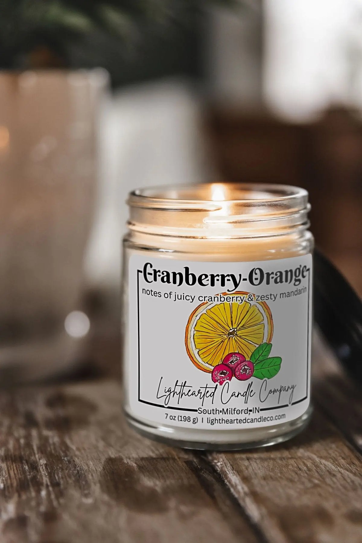 Lit Cranberry Orange Candle in a clear glass jar on a rustic wooden table