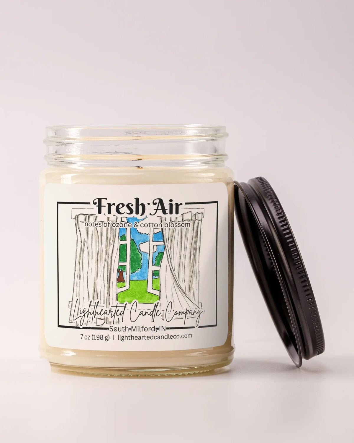 Unlit Fresh Air Candle in a clear glass jar with its black lid beside it