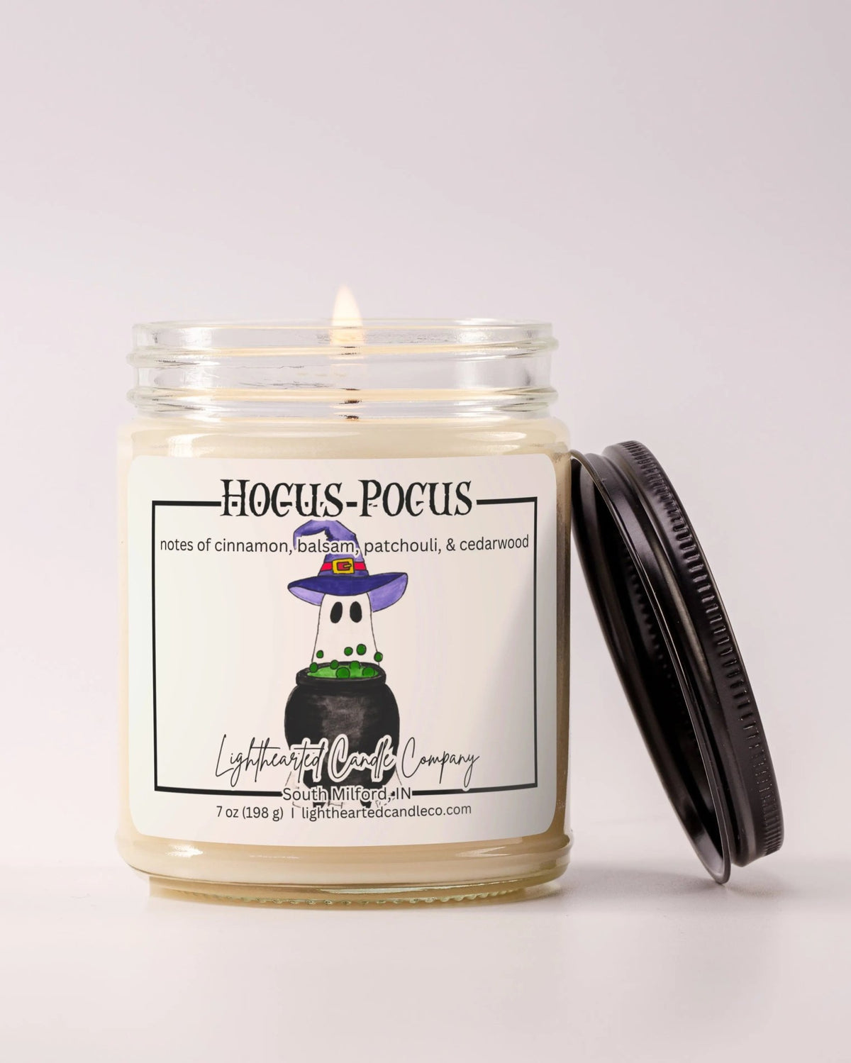 Lit Hocus Pocus Candle in a clear glass jar with its black lid beside it, alternate view 3