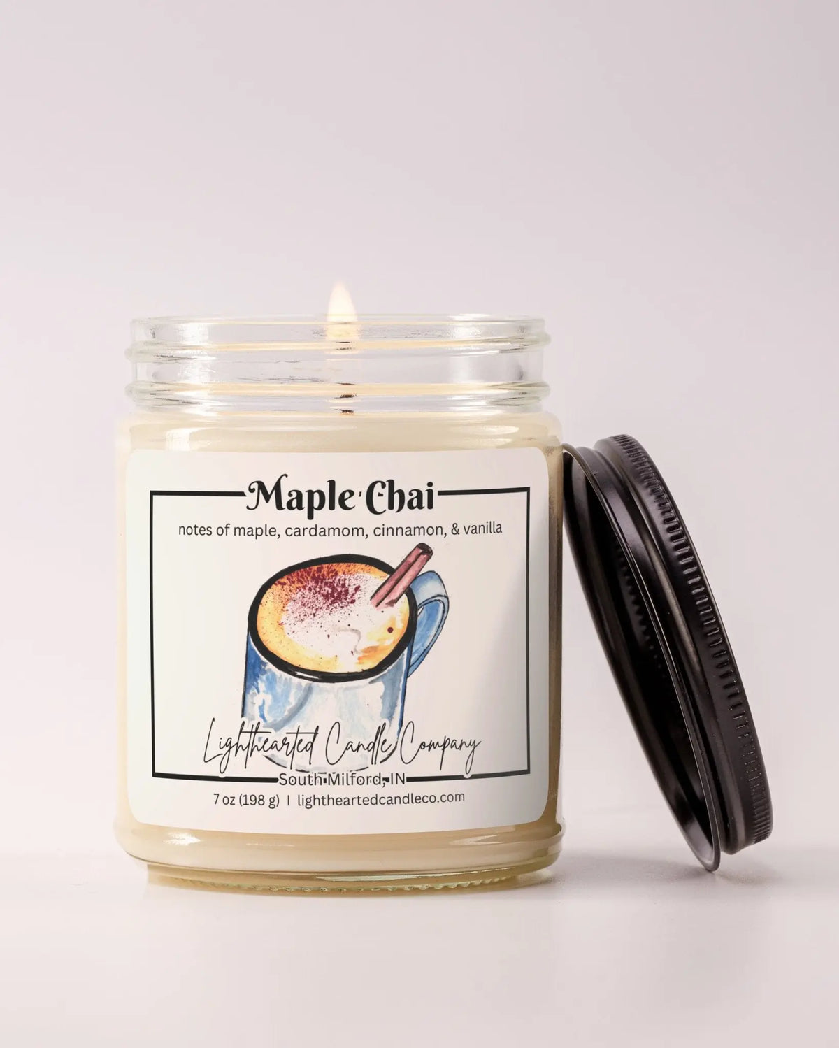 Lit Maple Chai Candle in a clear glass jar with its black lid beside it