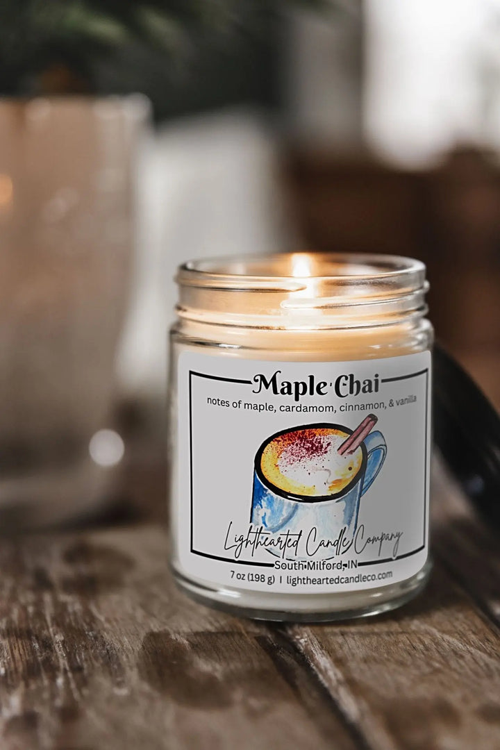 Lit Maple Chai Candle in a clear glass jar on a rustic wooden table