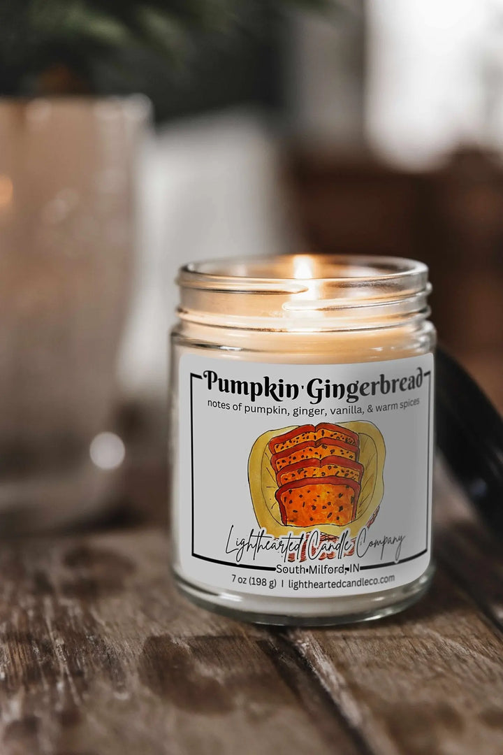 Lit Pumpkin Gingerbread Candle in a clear glass jar on a rustic wooden table