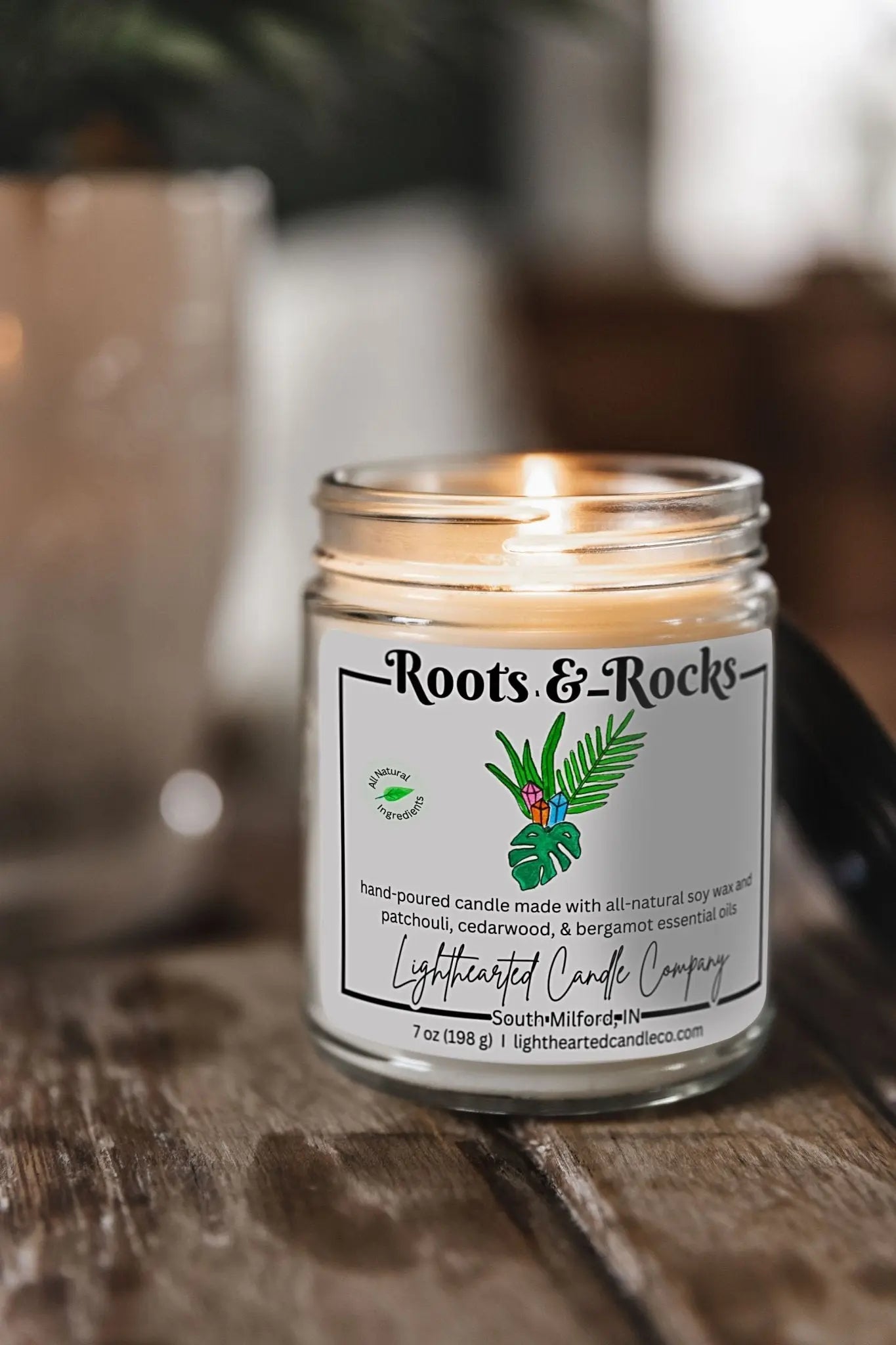 Lit Roots & Rocks Essential Oil Candle in a clear glass jar on a rustic wooden table