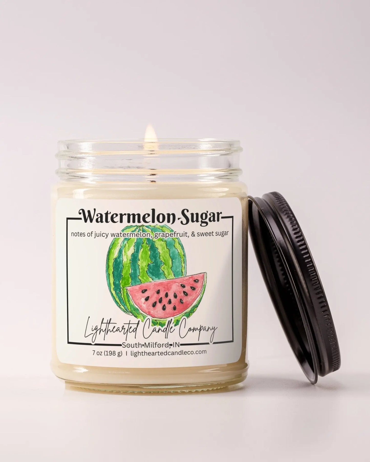 Lit Watermelon Sugar Candle in a clear glass jar with its black lid beside it