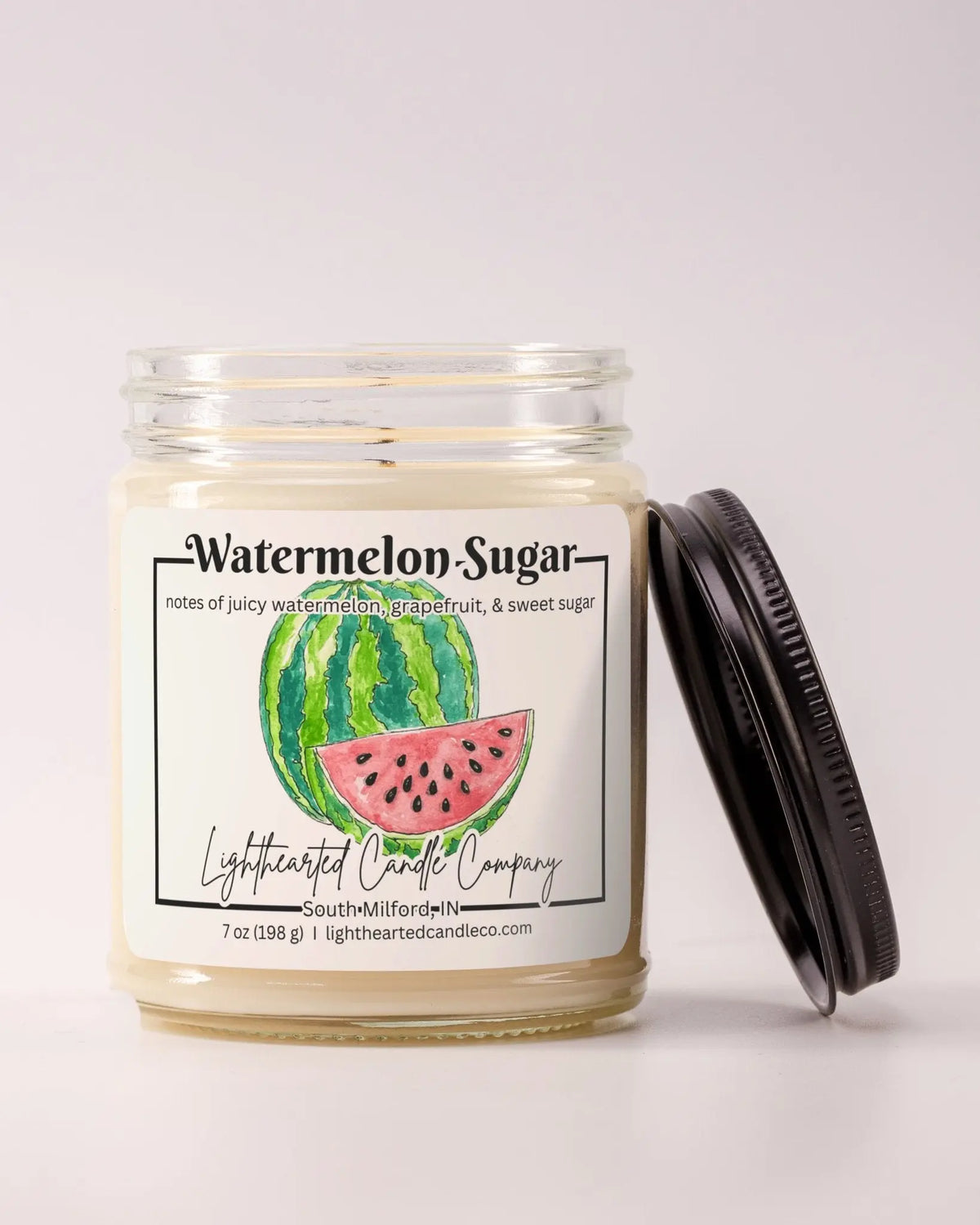 Unlit Watermelon Sugar Candle in a clear glass jar with its black lid beside it
